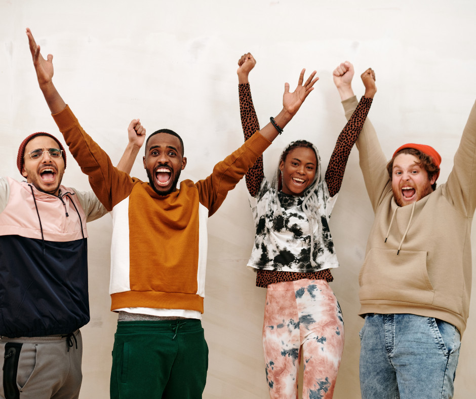Group of young adults 3 men and 1 women standing and cheering with their arms in the air